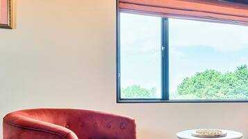 A room with a large window, a red upholstered chair, and a small round table with a decorative item.