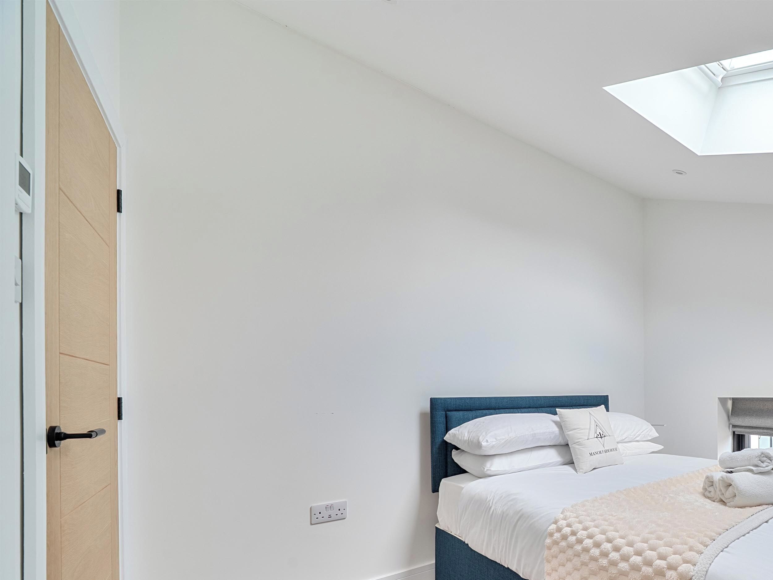 A bedroom with a bed, a skylight, a wooden door, and a white wall.