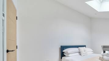 A bedroom with a bed, a skylight, a wooden door, and a white wall.