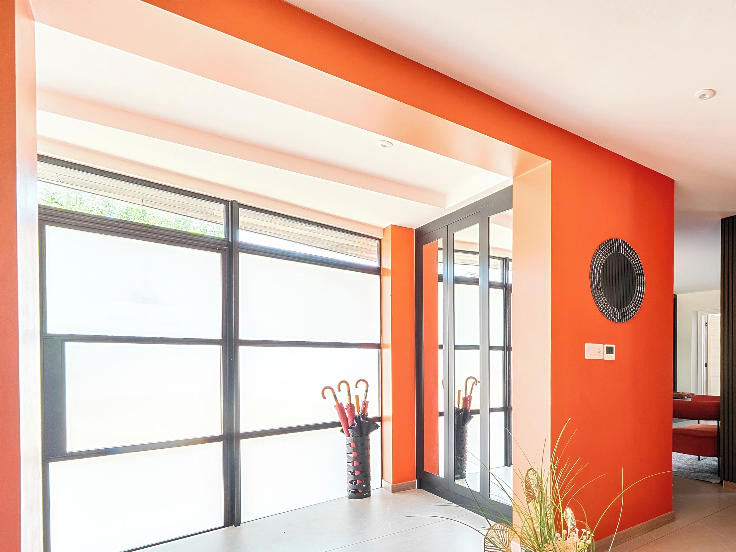 A modern interior with large windows, a red accent wall, and a decorative wall piece.