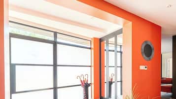 A modern interior with large windows, a red accent wall, and a decorative wall piece.