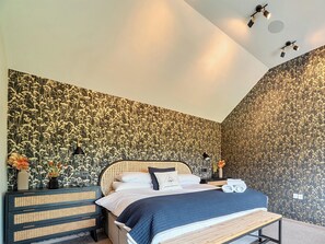 A bedroom with a bed, bedside tables, a wall with a floral pattern, and ceiling lights.