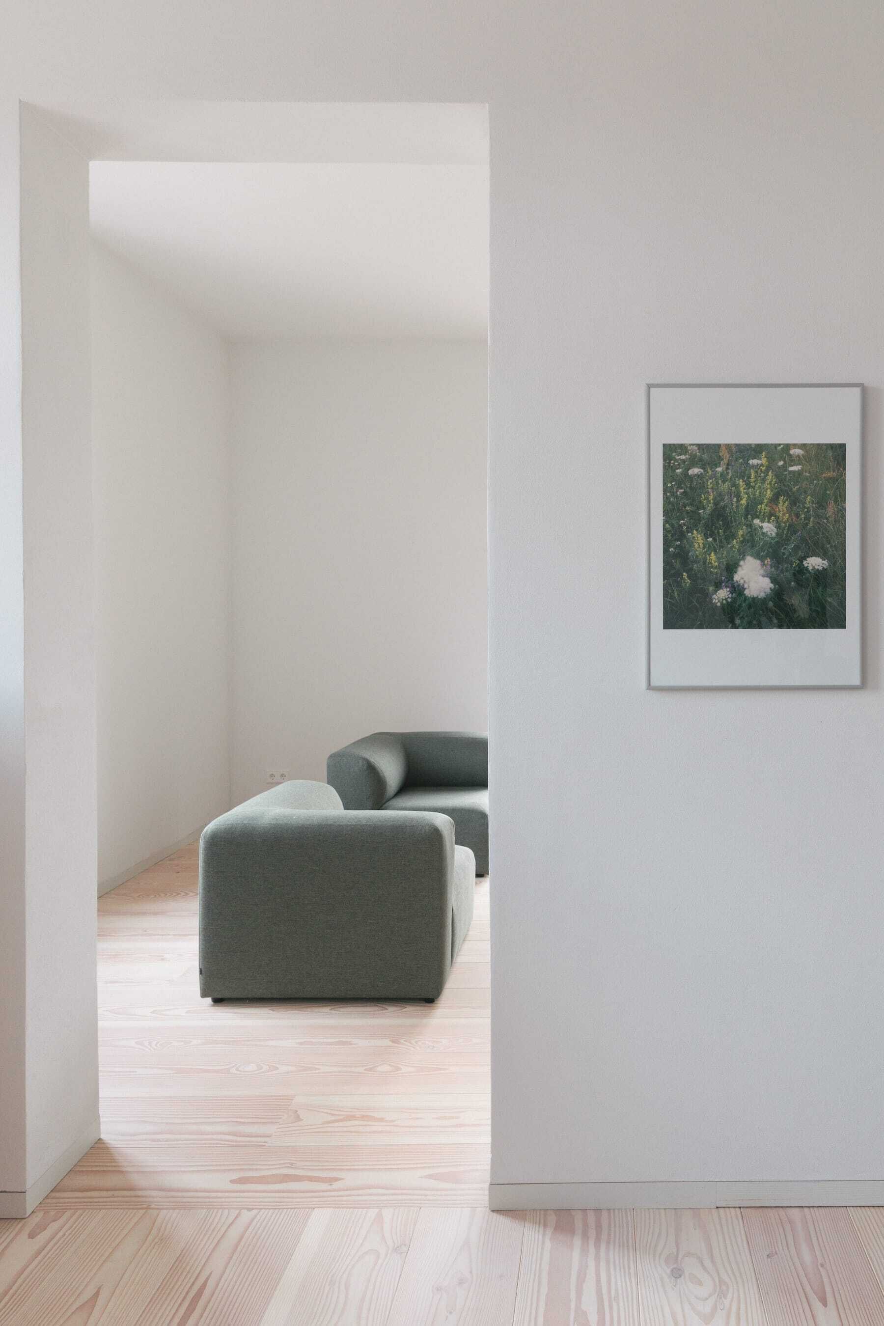 Une pièce au décor minimaliste, avec un canapé gris, un tableau encadré au mur et un plancher en bois.
