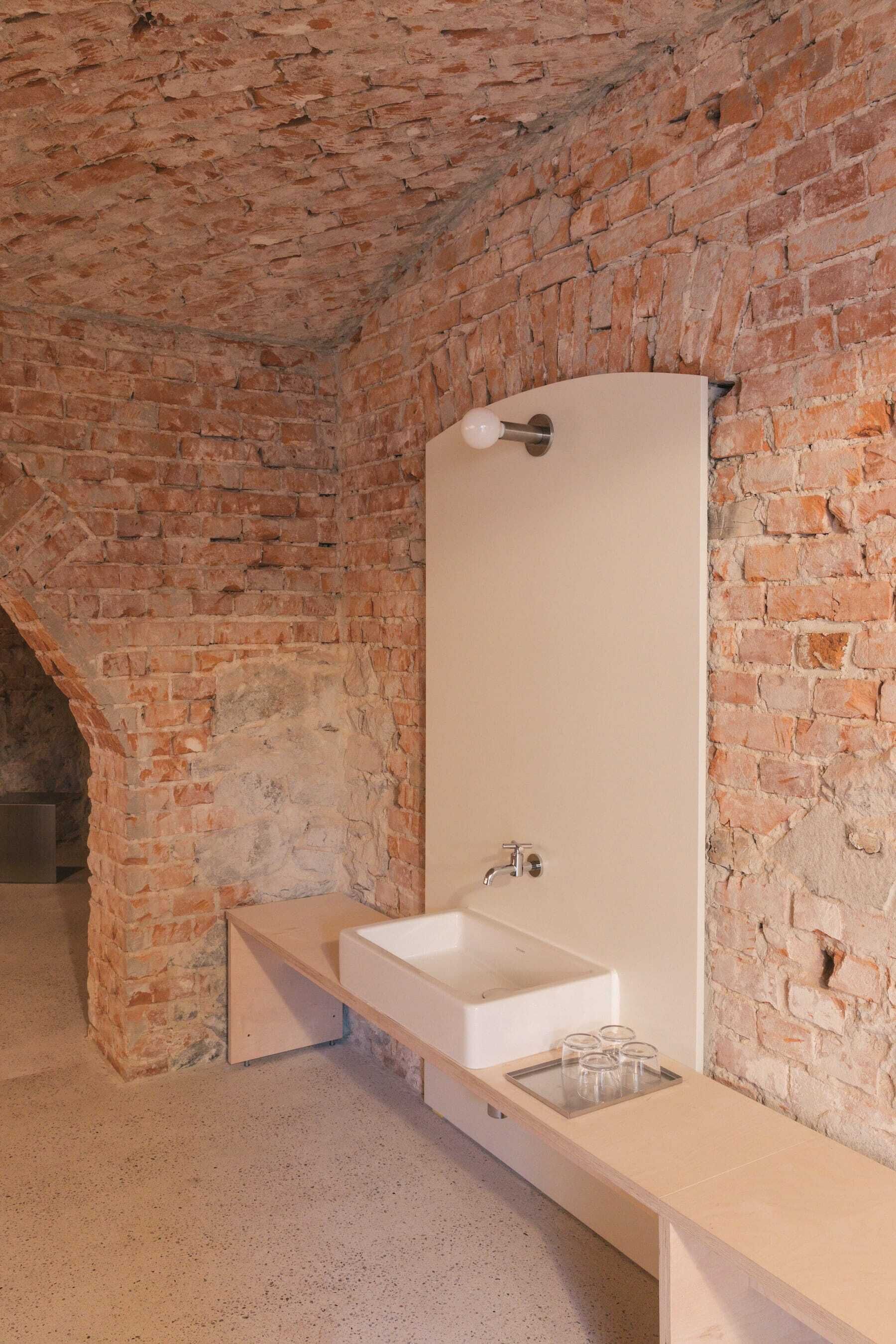Een badkamer met een witte wasbak, spiegel en een bakstenen muur.