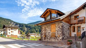 Ein Steinhaus mit einem hölzernen Balkon, einer Fußgängerampel und einem Berg im Hintergrund.