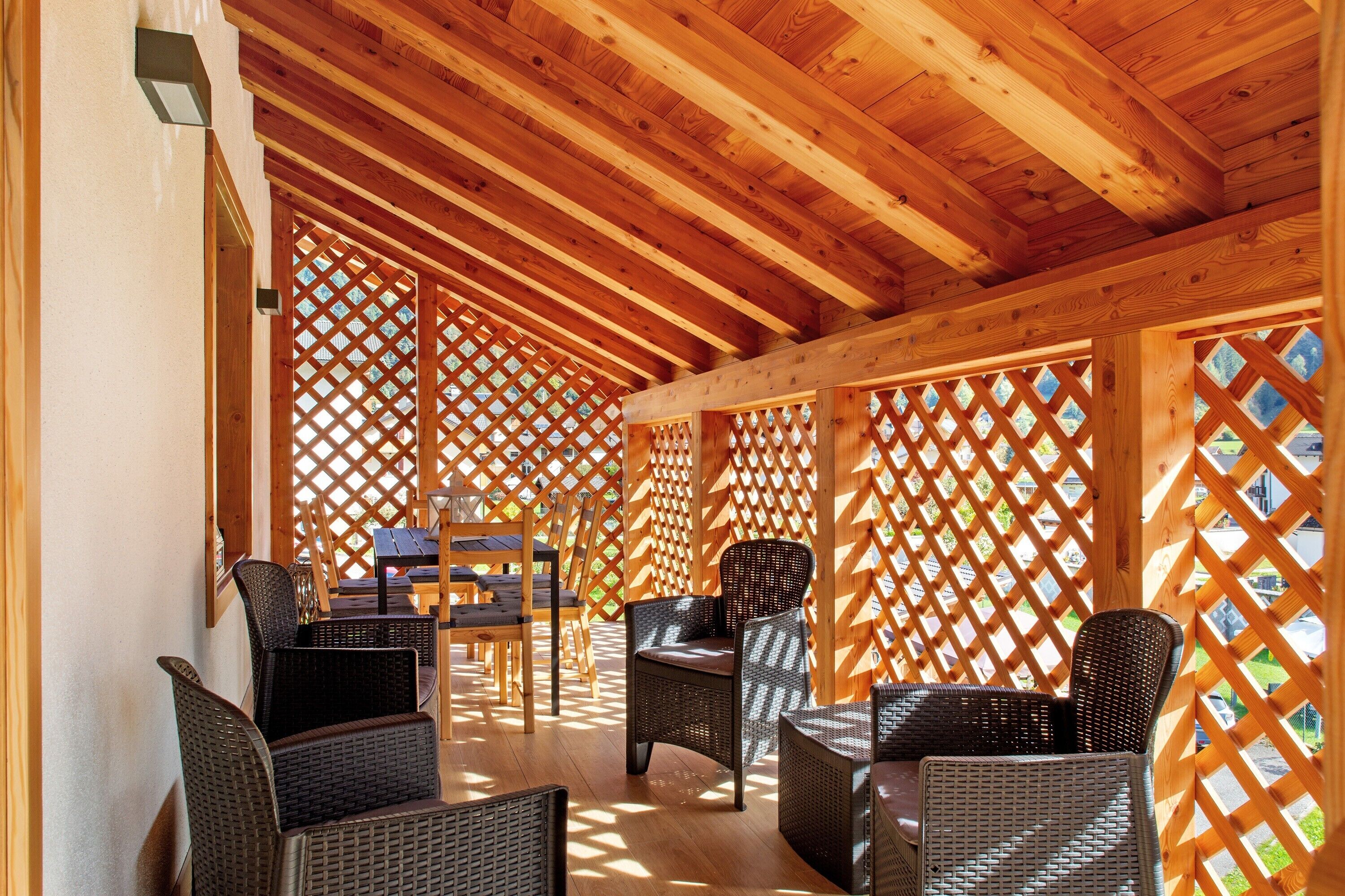 An indoor wooden structure with lattice walls, wicker furniture, and a table.