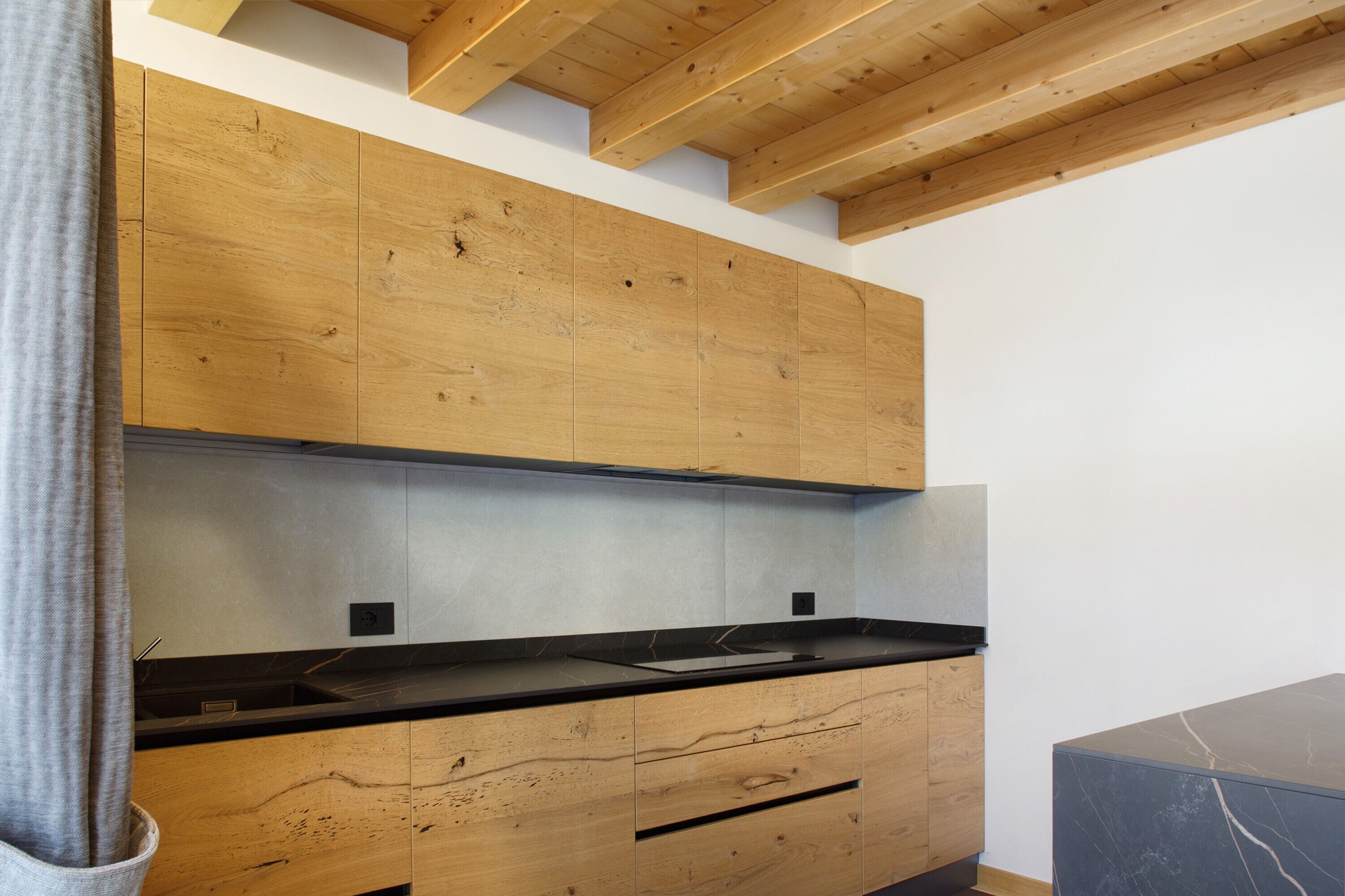 Een moderne keuken met houten kastjes, een zwart aanrecht en een marmeren achterwand.
