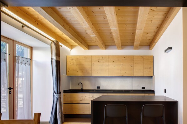 Une cuisine moderne avec des meubles en bois, un plan de travail noir et un coin repas comprenant une table et des chaises.