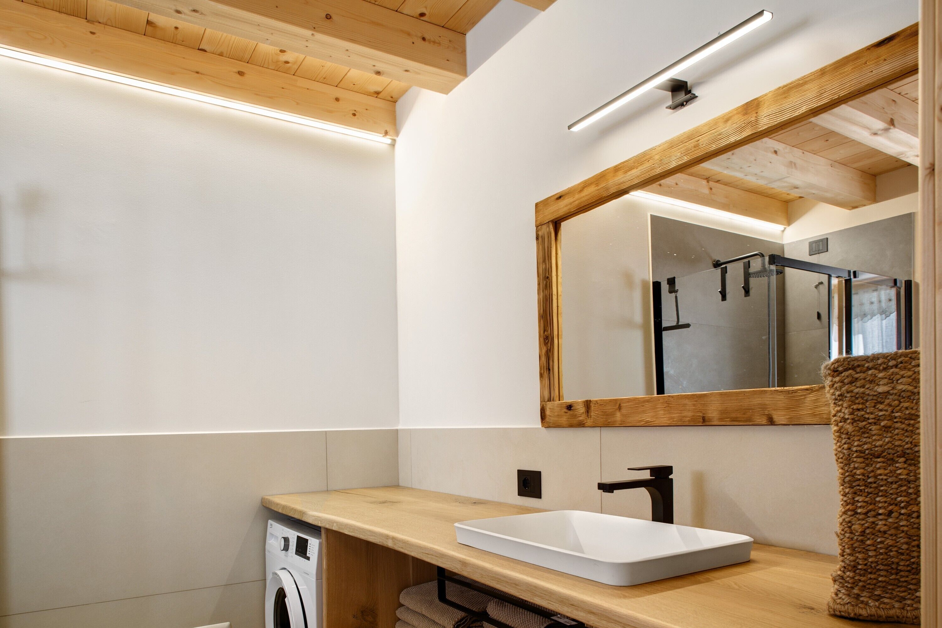 Ein modernes Badezimmer mit Waschtisch aus Holz, einer weißen Spüle, einem Spiegel und einer Waschmaschine.