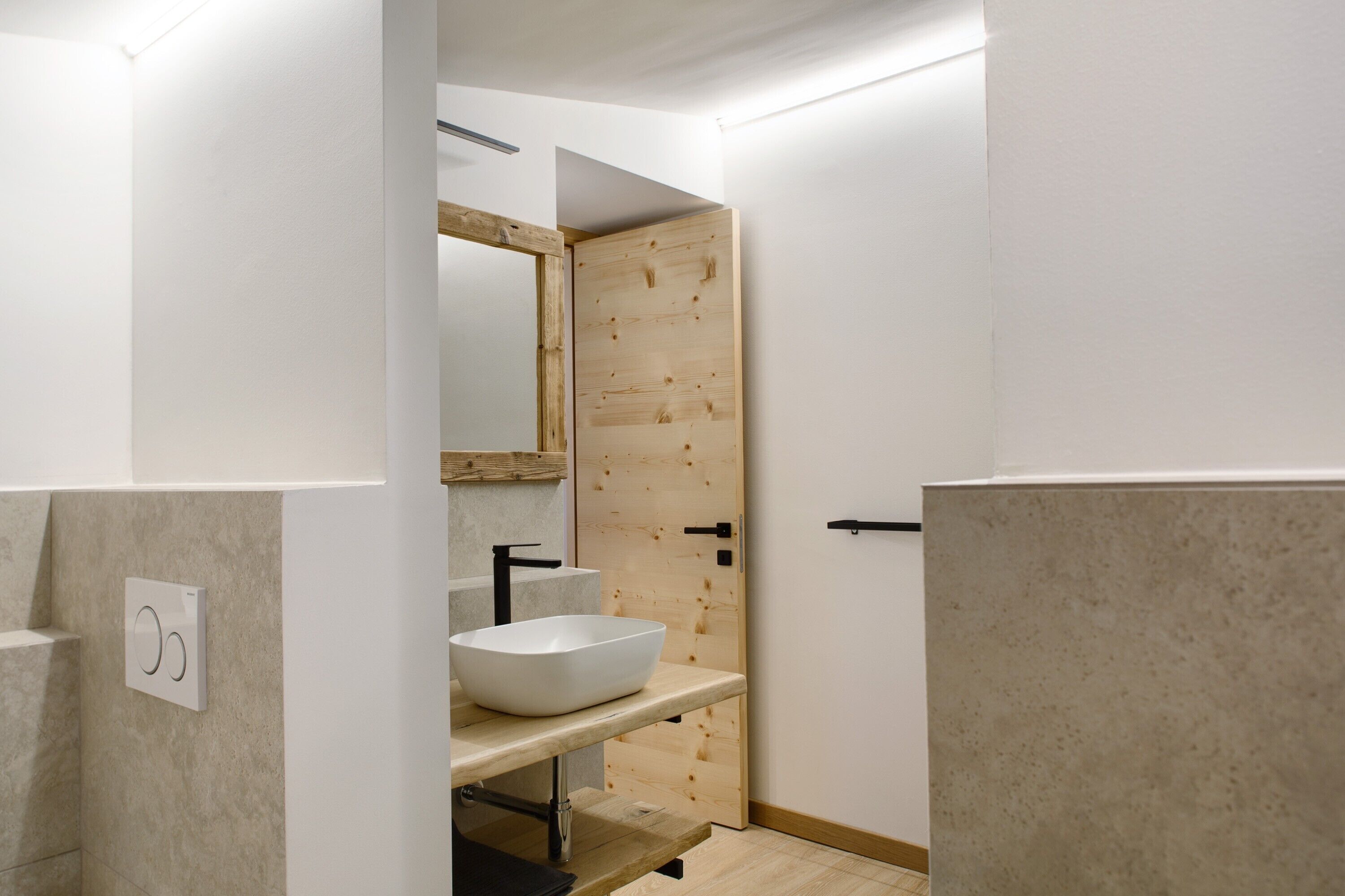 Ein modernes Badezimmer mit Holztür, weißem Waschbecken und Spiegel.