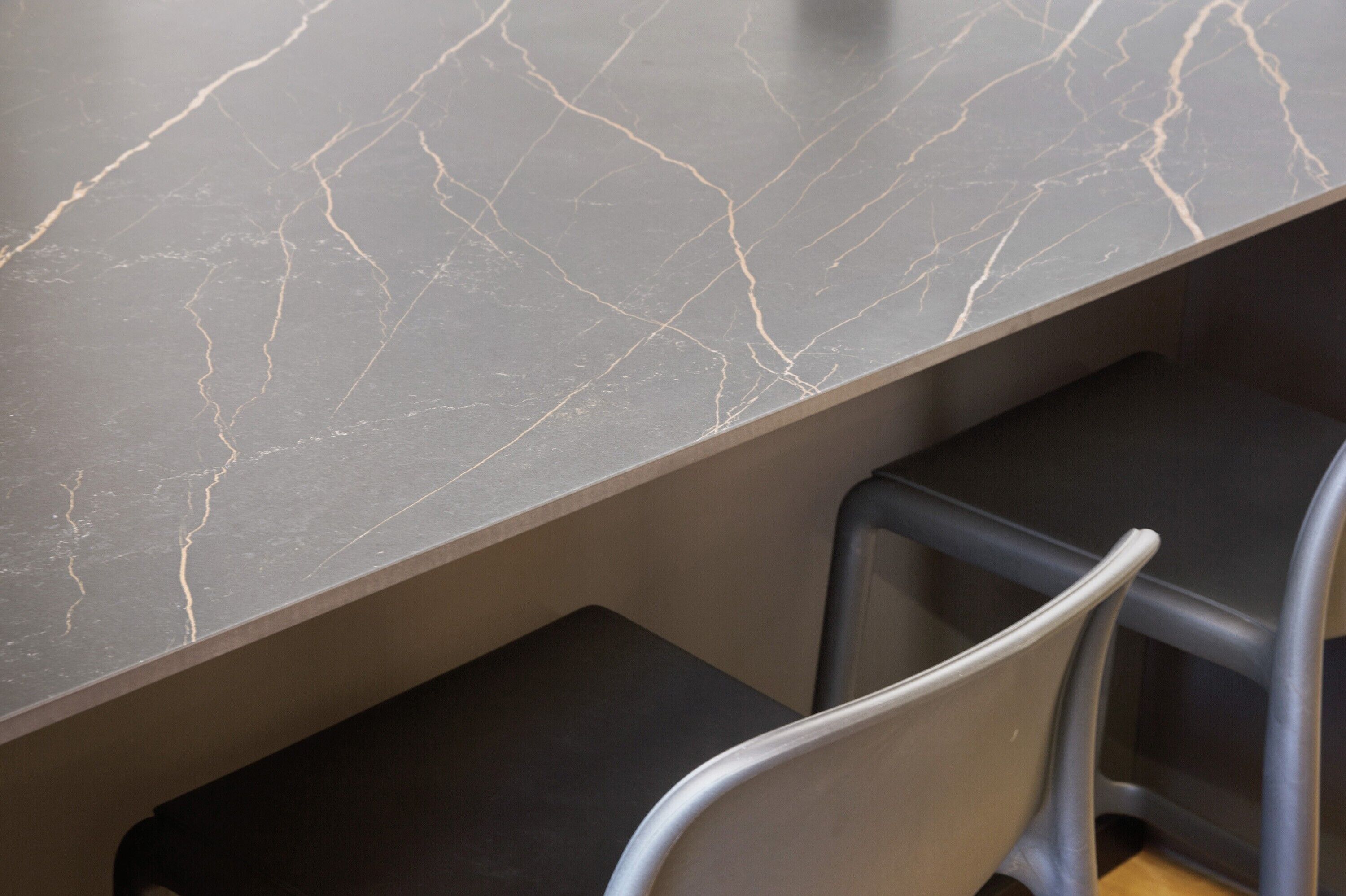 Een moderne bar met een marmeren aanrecht en metalen stoelen.