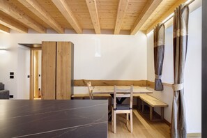 Een kamer met een houten plafond, een zwarte tafel, een houten bank en een gordijn.