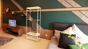 A modern living room with a sectional sofa, a white shelving unit, a television, and a patterned wall. - The Miere Suites @ KLIA Sepang (Sepang)