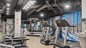Uma academia com esteiras, aparelhos de musculação e um painel de espelhos.