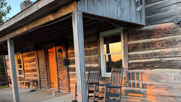 Eine rustikale Holzhütte mit Veranda, Sitzgelegenheiten im Freien und einem Garten mit Sonnenblumen.