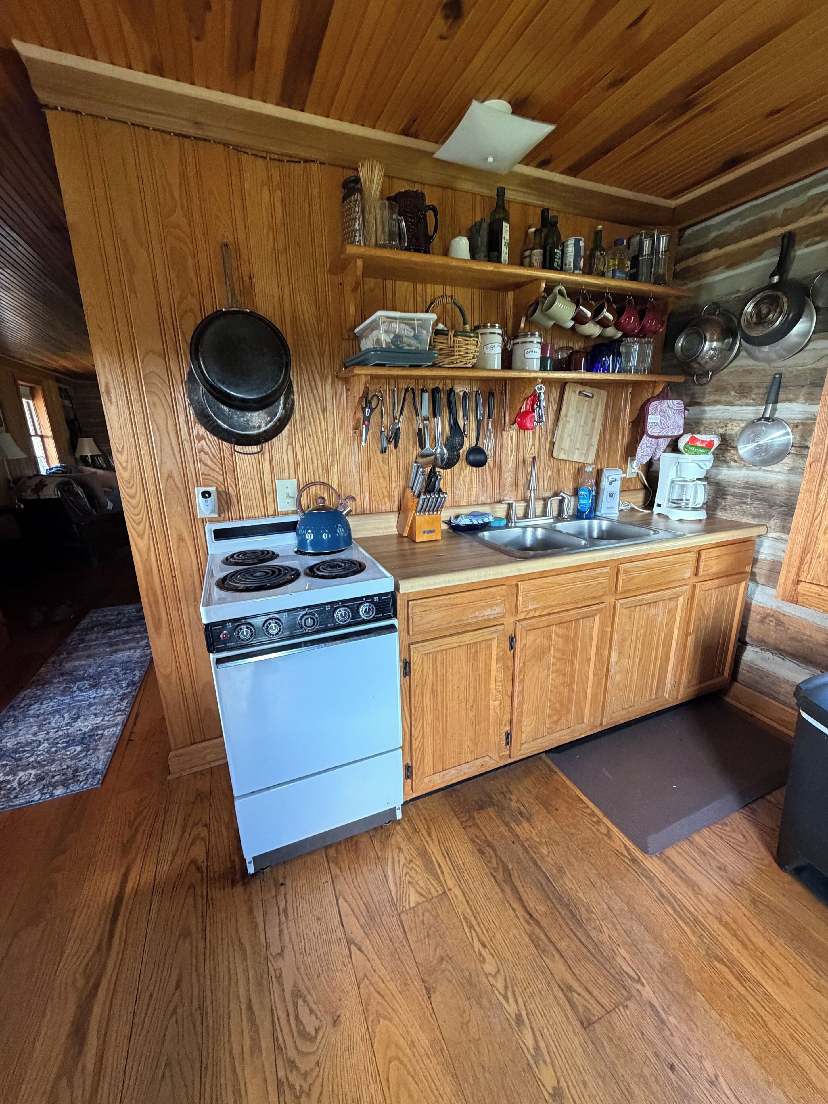 A compact kitchen with wooden cabinets, a stove, and various utensils hanging on the wall.