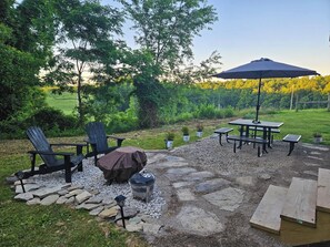 Patio esterno con poltrone Adirondack, barbecue coperto, tavolo con panche e un ombrellone grande.