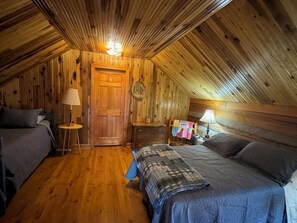 Ein gemütliches Schlafzimmer im Dachgeschoss mit Holzwänden und geneigter Decke, ausgestattet mit zwei Betten, einem Schminktisch und einer Tür.