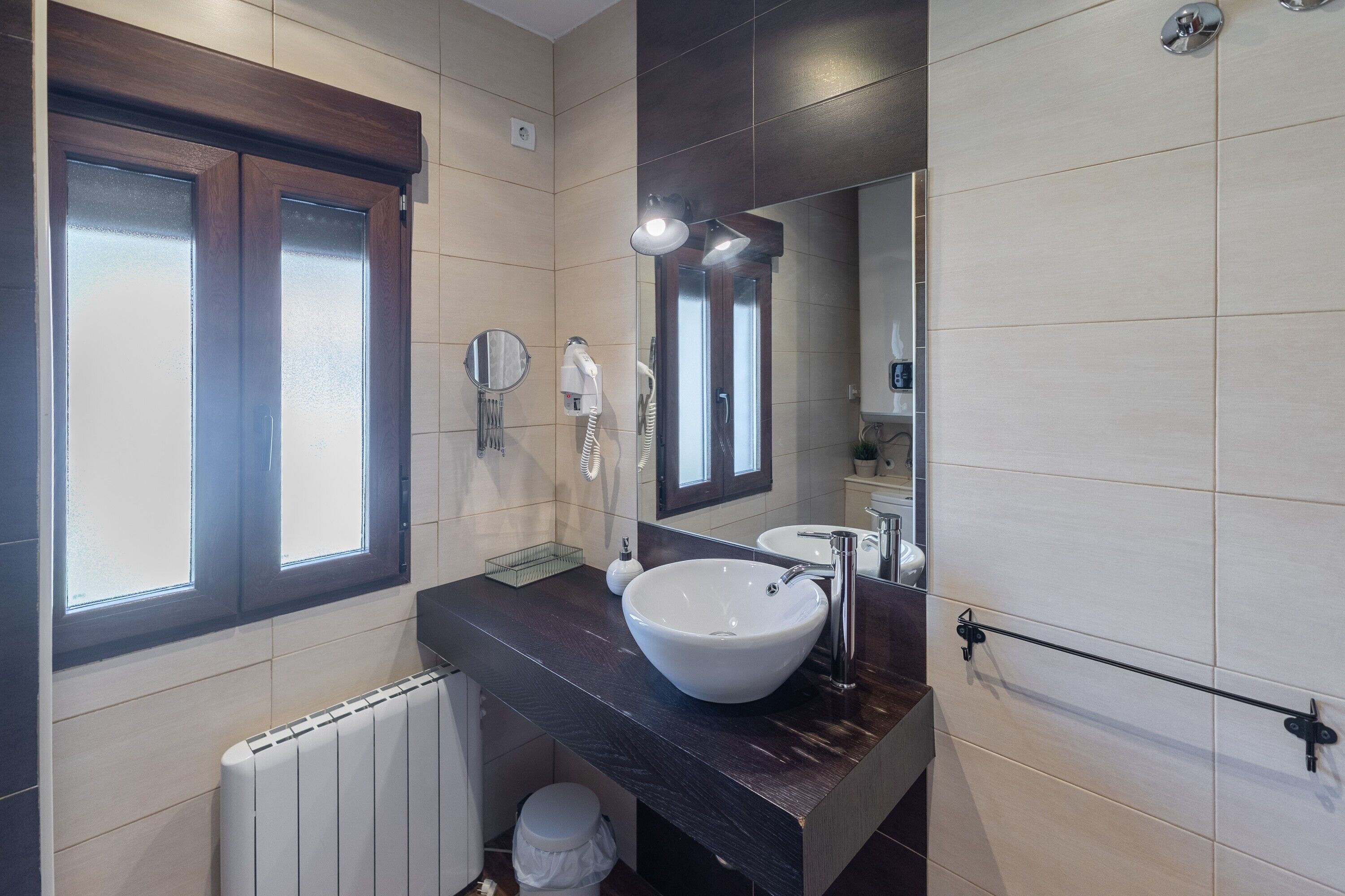 Une salle de bain moderne avec un grand miroir, un lavabo blanc, un sèche-cheveux et un porte-serviettes.