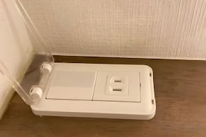A white electrical outlet box with two sockets, located on a wooden floor against a textured wall. - (Male Only)BEE-HIVE Sugamo (Tokyo)