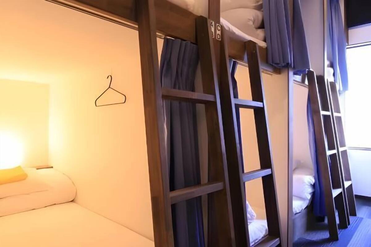 A bunk bed room with a hanging clothes rack, a bedside table, and a window with curtains.