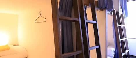 A bunk bed room with a hanging clothes rack, a bedside table, and a window with curtains.