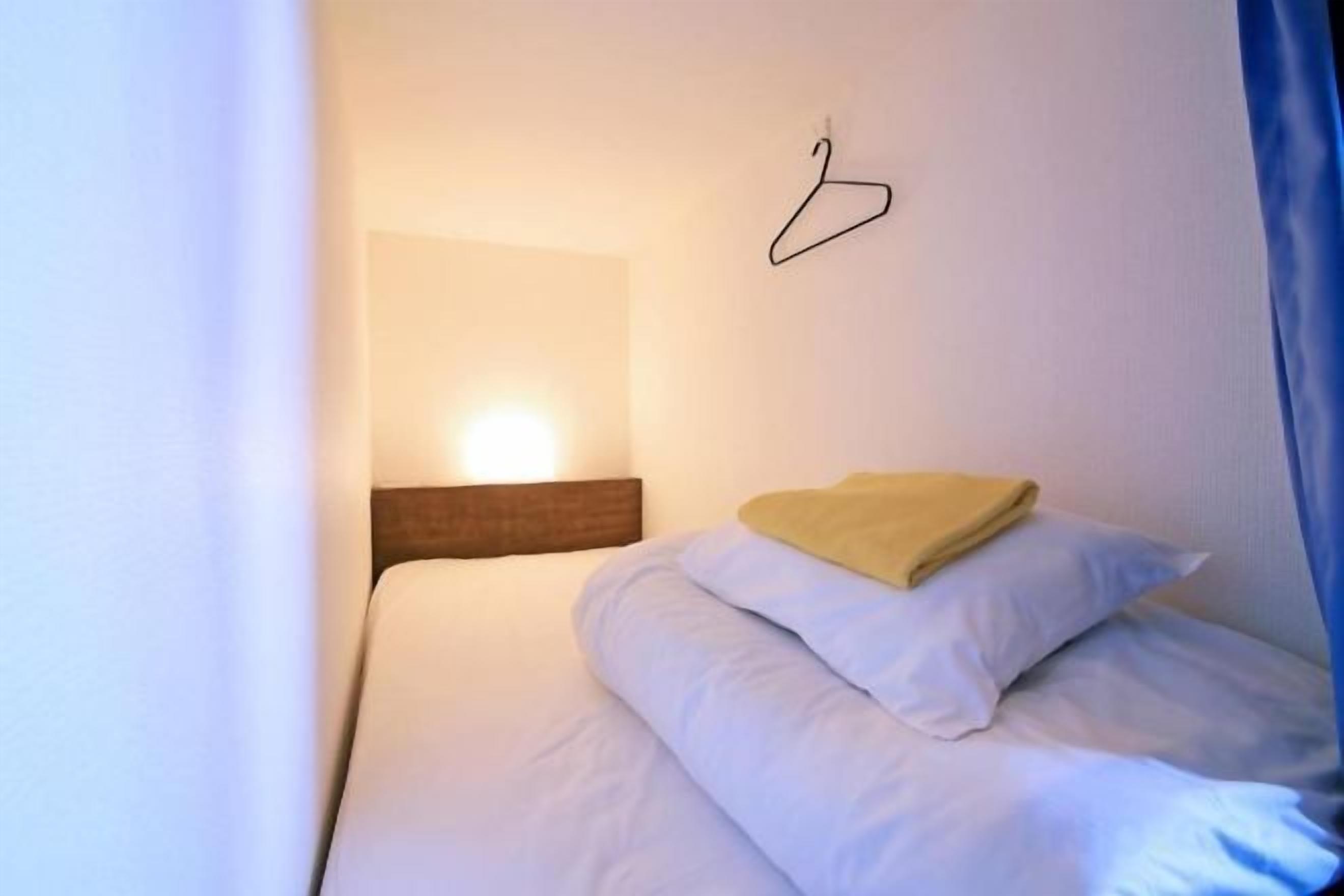 A single bed with white bedding, a hanging light fixture, and a blue curtain.