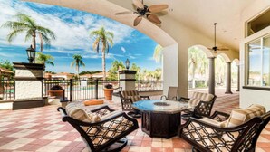 A covered patio with outdoor furniture, a ceiling fan, and a view of palm trees and a pool. - Bella Vida Cozy Home | 15 min to Disney | Resort Style (Kissimmee)