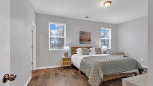 A bedroom with a bed, nightstands, a window, and a painting. - Stylish & Spotless 4BR - Backyard, Grill, Near the Beach (Myrtle Beach)