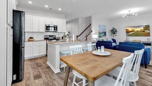 A modern kitchen with white cabinets, a black refrigerator, and a wooden dining table with white chairs. - Stylish & Spotless 4BR - Backyard, Grill, Near the Beach (Myrtle Beach)