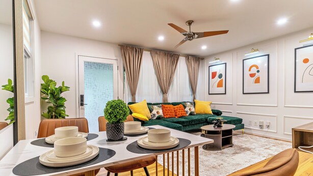 A modern living room with a green sofa, brown leather chairs, a dining table with white plates, and a ceiling fan. - Limited time Deal! Cozy Luxe Escape Modern 2BR, sleeps 4,Couples, Business & Pet (Raleigh)