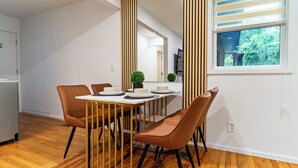 A modern dining area with a white table and brown chairs, a small potted plant, and a window with a view of greenery. - Limited time Deal! Cozy Luxe Escape Modern 2BR, sleeps 4,Couples, Business & Pet (Raleigh)