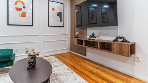 A modern living room with a wooden floor, a round coffee table, a green sofa, and a mounted TV. - Limited time Deal! Cozy Luxe Escape Modern 2BR, sleeps 4,Couples, Business & Pet (Raleigh)