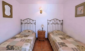 A bedroom with two beds, a nightstand with a lamp, a clock, and a wall-mounted light fixture.