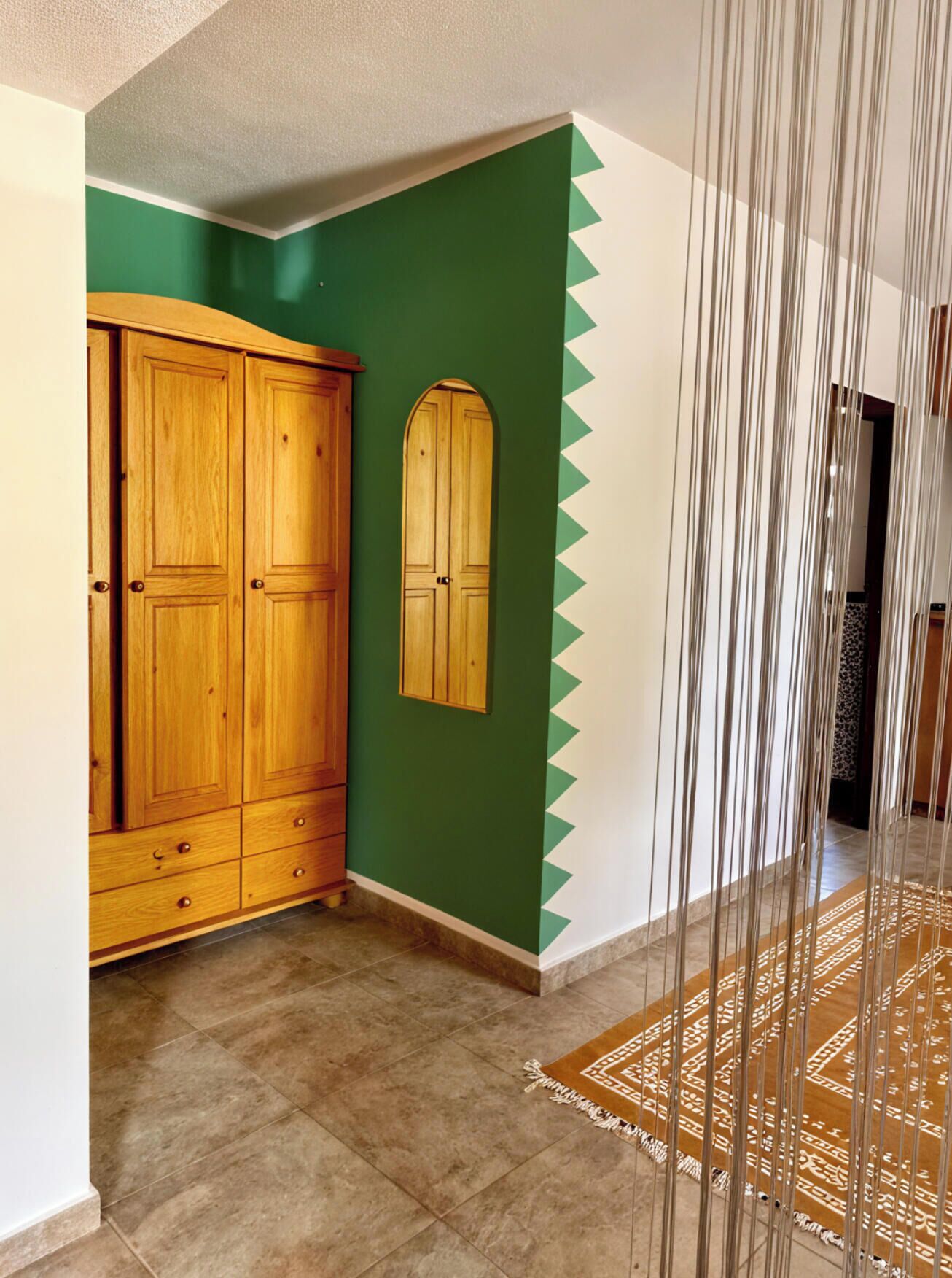 A hallway with a wooden wardrobe, a green accent wall, and a patterned rug.
