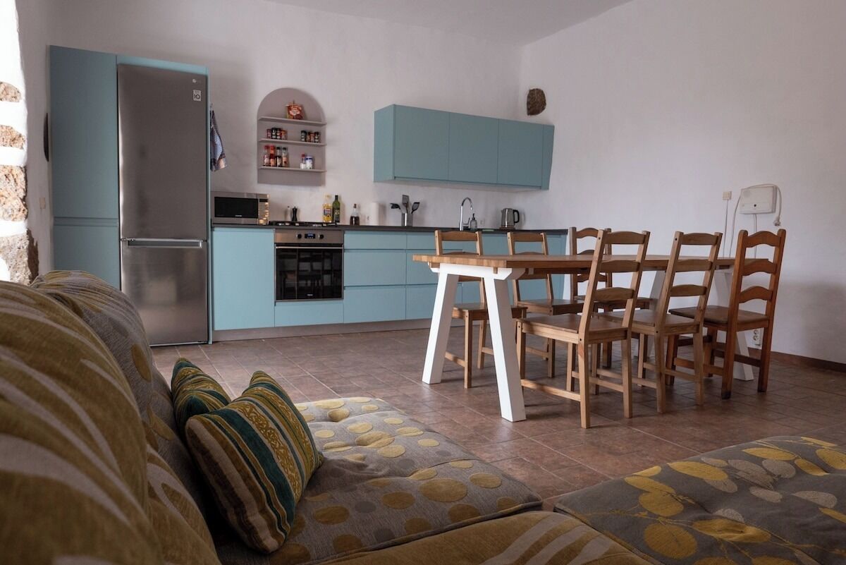 Eine kompakte Küche mit türkisfarbenen Schränken, einem Edelstahl-Kühlschrank und einem Essbereich mit Holztisch und Stühlen.