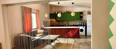 A modern kitchen with green cabinets, a red chair, and a dining area with a table and curtains.