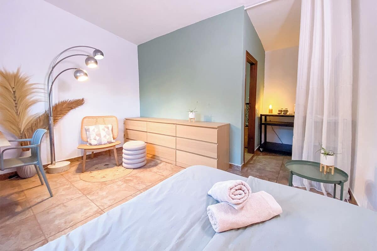 A modern bedroom with a bed, a dresser, a chair, and a lamp.