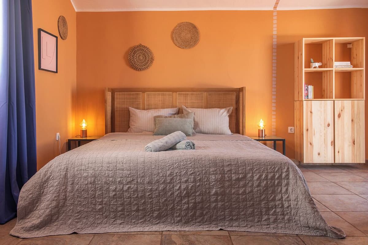A bedroom with a large bed, two bedside tables with lamps, a wooden wardrobe, and decorative wall hangings.