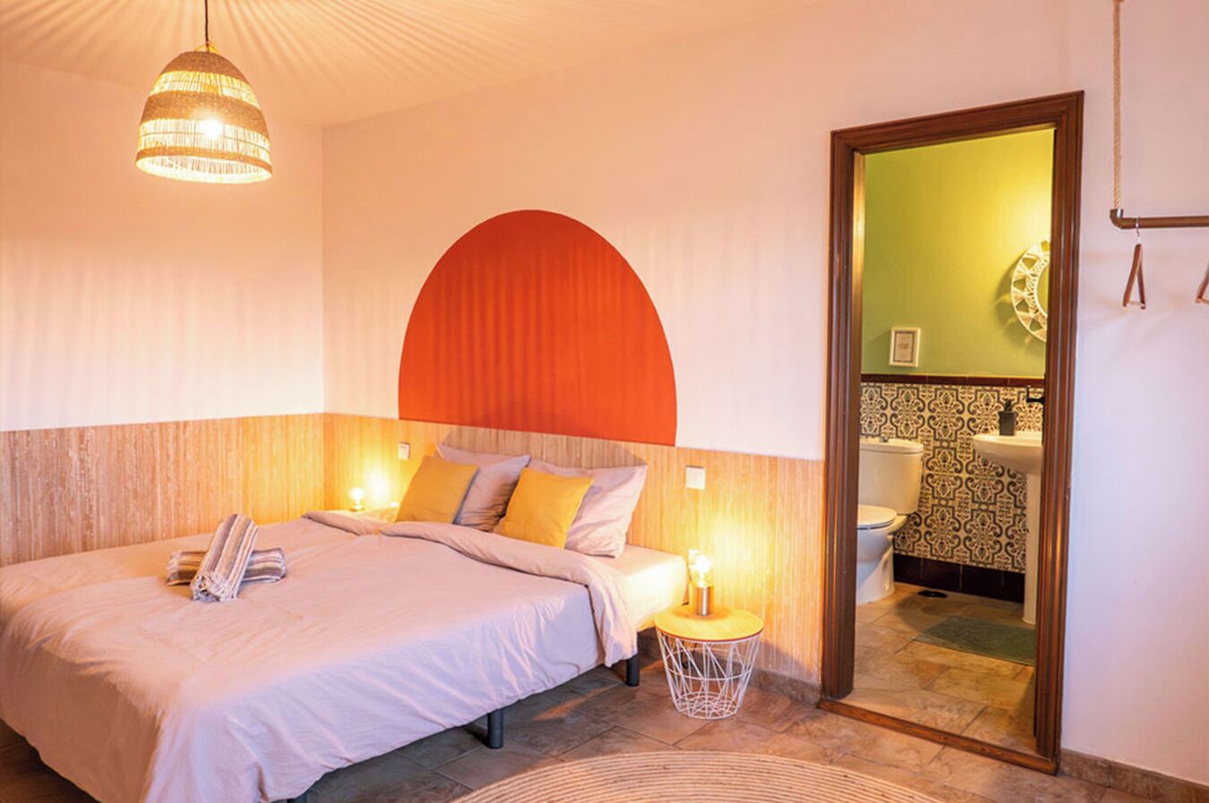 Quarto de hotel com cama, abajures, um espelho redondo e vista para o banheiro.