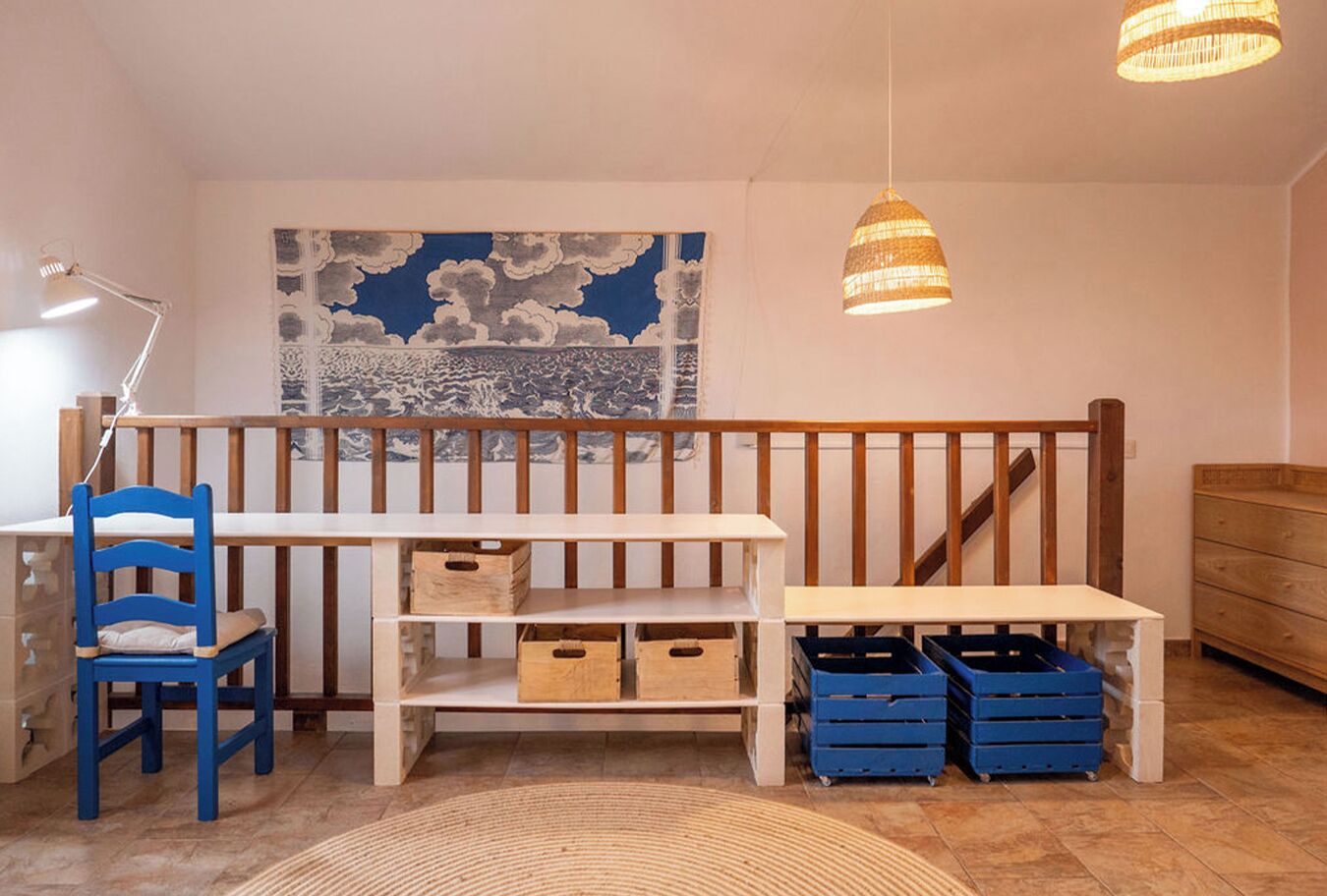 A room with a wooden bench, a blue chair, a white desk, and a wall with a cloud-patterned tapestry.