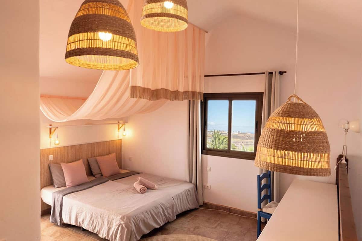 A bedroom with a bed, bedside lamps, a window, and a hanging light fixture.