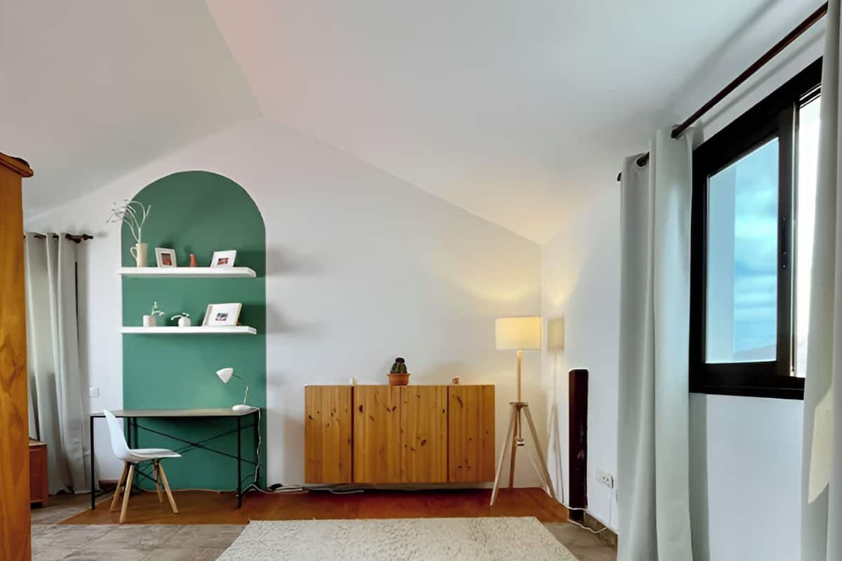 A bedroom with a bed, a desk, a green wall, and a window.
