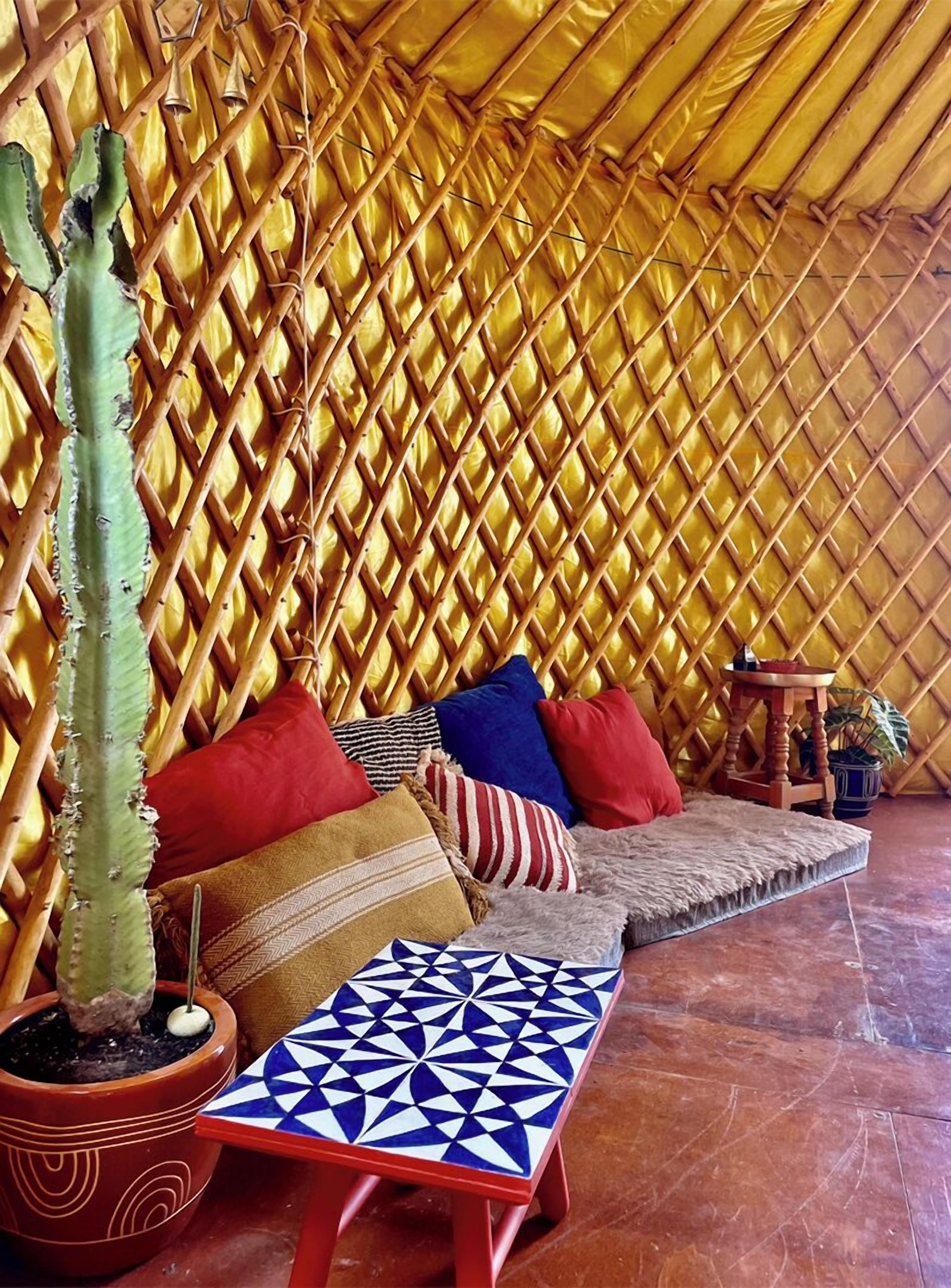 Una habitación con pared de bambú trenzado, un cactus, un sofá con cojines de colores y una mesa con estampado.