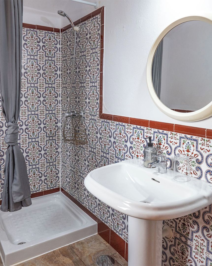 A bathroom with a shower, a sink, a mirror, and patterned tiles.