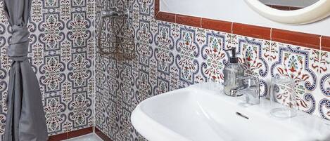 A bathroom with a shower, a sink, a mirror, and patterned tiles.