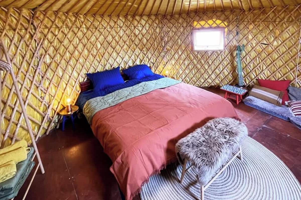 A yurt with a bed, a small table, and a rug.