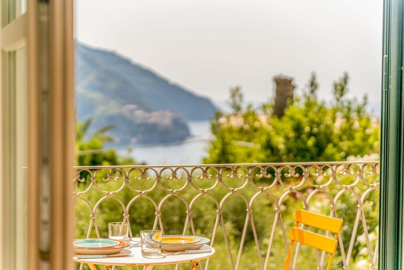 A balcony with a table set for two, overlooking a body of water and greenery.