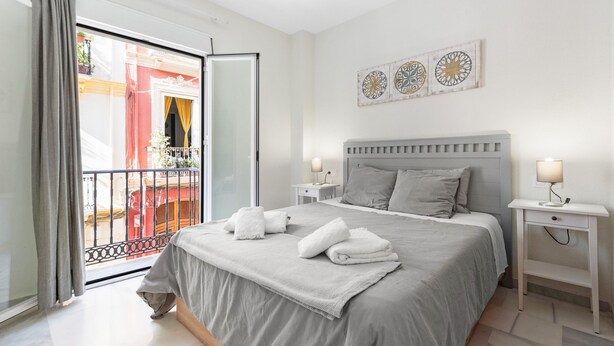 A hotel room with a bed, two bedside tables, a nightstand, a balcony with a view, and decorative wall art. - 'Apartamento Mariblanca 6' with Balcony, Wi-Fi and Air Conditioning (Málaga)