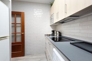 Une cuisine avec des murs recouverts de carreaux blancs, des meubles en bois, un plan de travail noir et un four encastré.